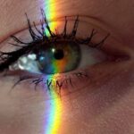 Creative Minds - Closeup of crop anonymous sad female with green eyes and rainbow light on face looking at camera
