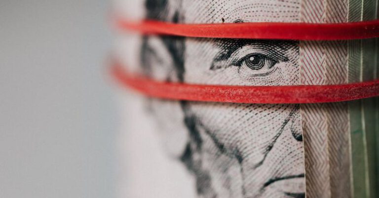 Exchange Rates - Closeup of rolled United States five dollar bills tightened with red rubber band